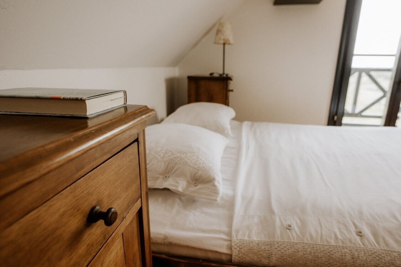 Et soveværelse med et træmøbel, en seng med hvide sengetæpper, et natbord med lampe og et vindue med udsigt.