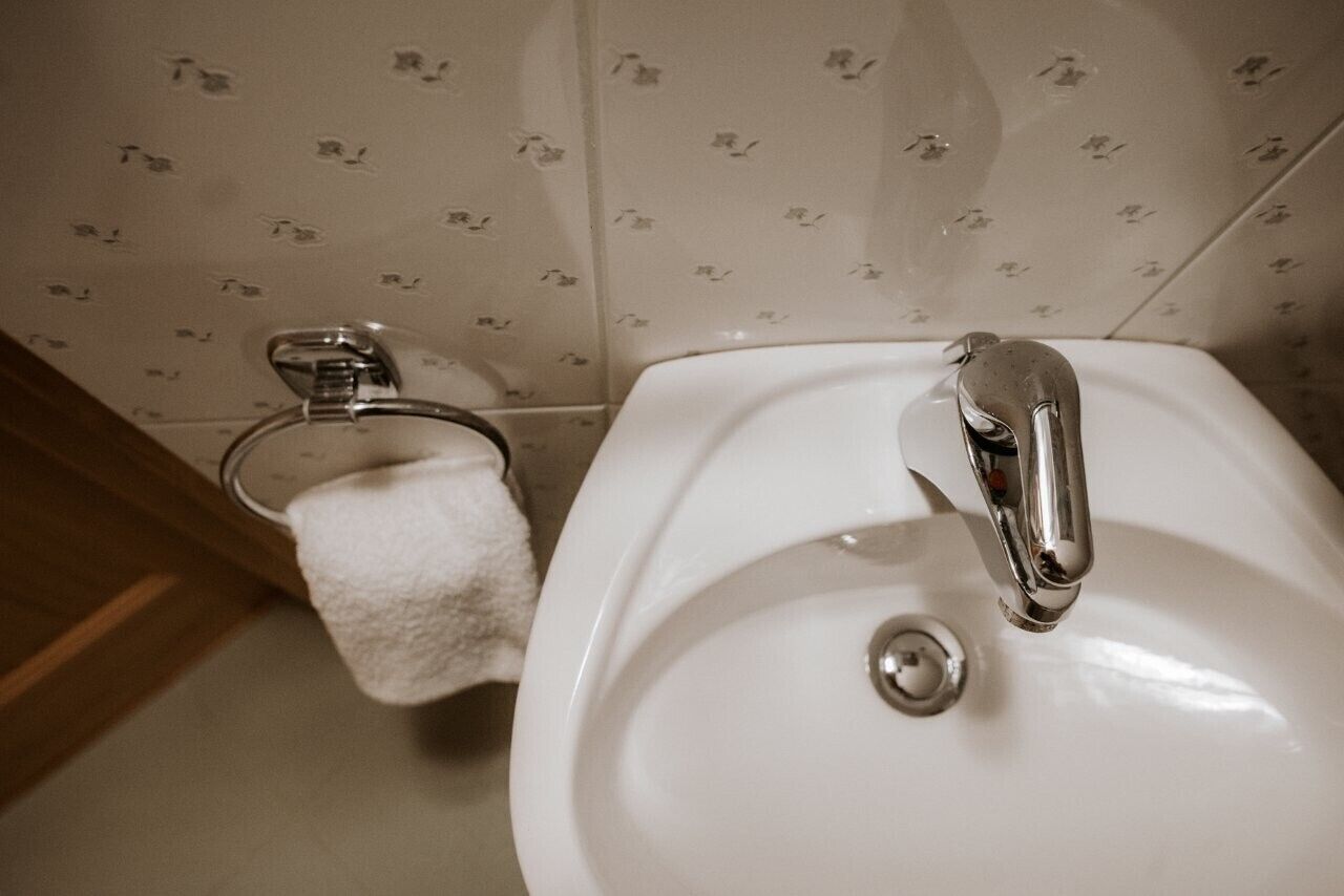 A bathroom with a white sink, chrome faucet, and a toilet with a white towel.
