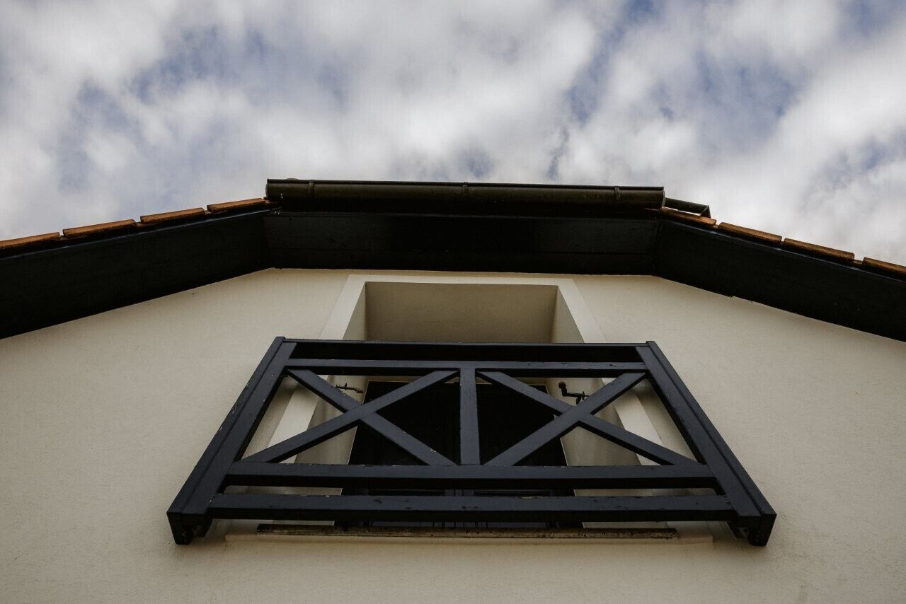 A corner of a building with a black metal frame window and a beige wall.