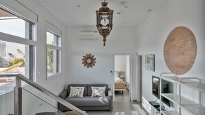 Uma sala de estar ampla, com um sofá cinzento, um espelho decorativo em forma de sol e uma grande parede de tijolos.