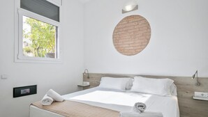 Quarto de hotel moderno com uma cama grande, uma parede decorativa de tijolos arredondada, uma janela com vista para o verde e um painel de controle na parede.
