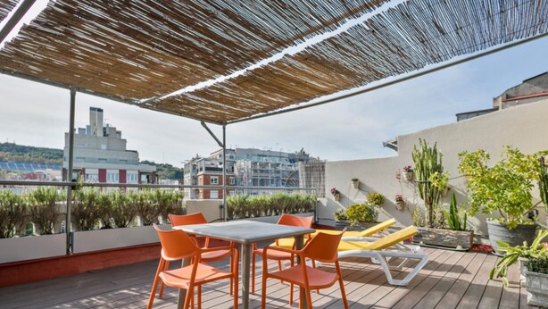 Terraço no telhado com mesa e cadeiras, plantas em vasos e vista para a paisagem urbana.