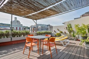 Una terraza en la azotea con mesa y sillas, plantas en macetas y vistas de la ciudad.