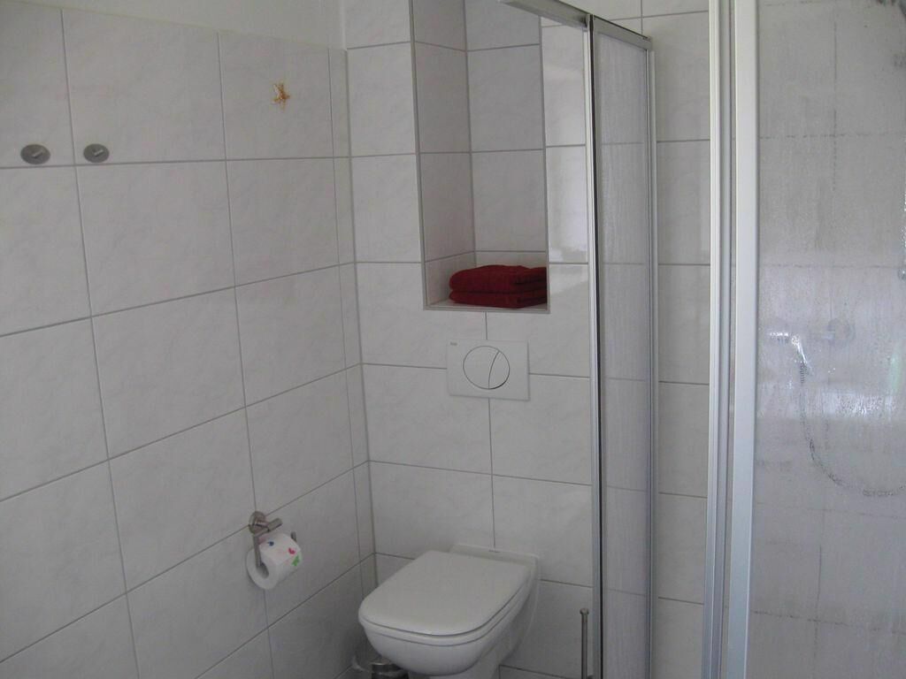 A bathroom with a toilet, a shower enclosure, and a red towel on a shelf.