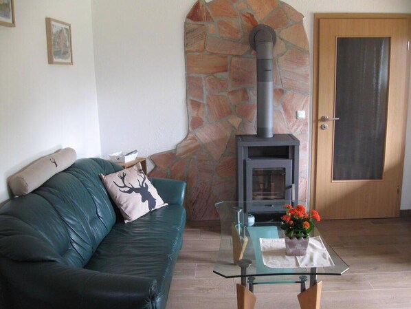 A living room with a stone wall, a sofa, a glass coffee table with a flower vase, and a wood-burning stove. - Des Försters Ferienhaus - Haus Hirsch (Jamel, südliches Mecklenburg)