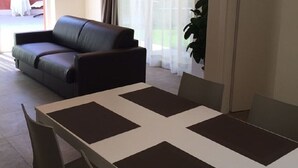 A modern living room with a dark leather sofa, a dining table with four chairs, and a large window with sheer curtains. - Villa Rossa Dependance Lake Garda Bardolino-Cavaion (Dependance) (Cavaion Veronese)