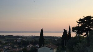 A coastal town with houses, cypress trees, and a view of the sea at sunset. - Villa Rossa Dependance Lake Garda Bardolino-Cavaion (Dependance) (Cavaion Veronese)
