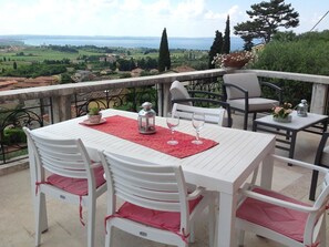 A terrace with a white table and chairs, a red placemat, and a view of a landscape with trees and a body of water.