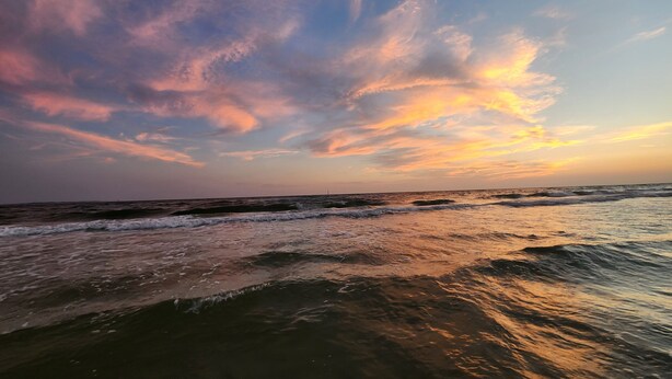 Uma praia com ondas e um céu ao pôr do sol.