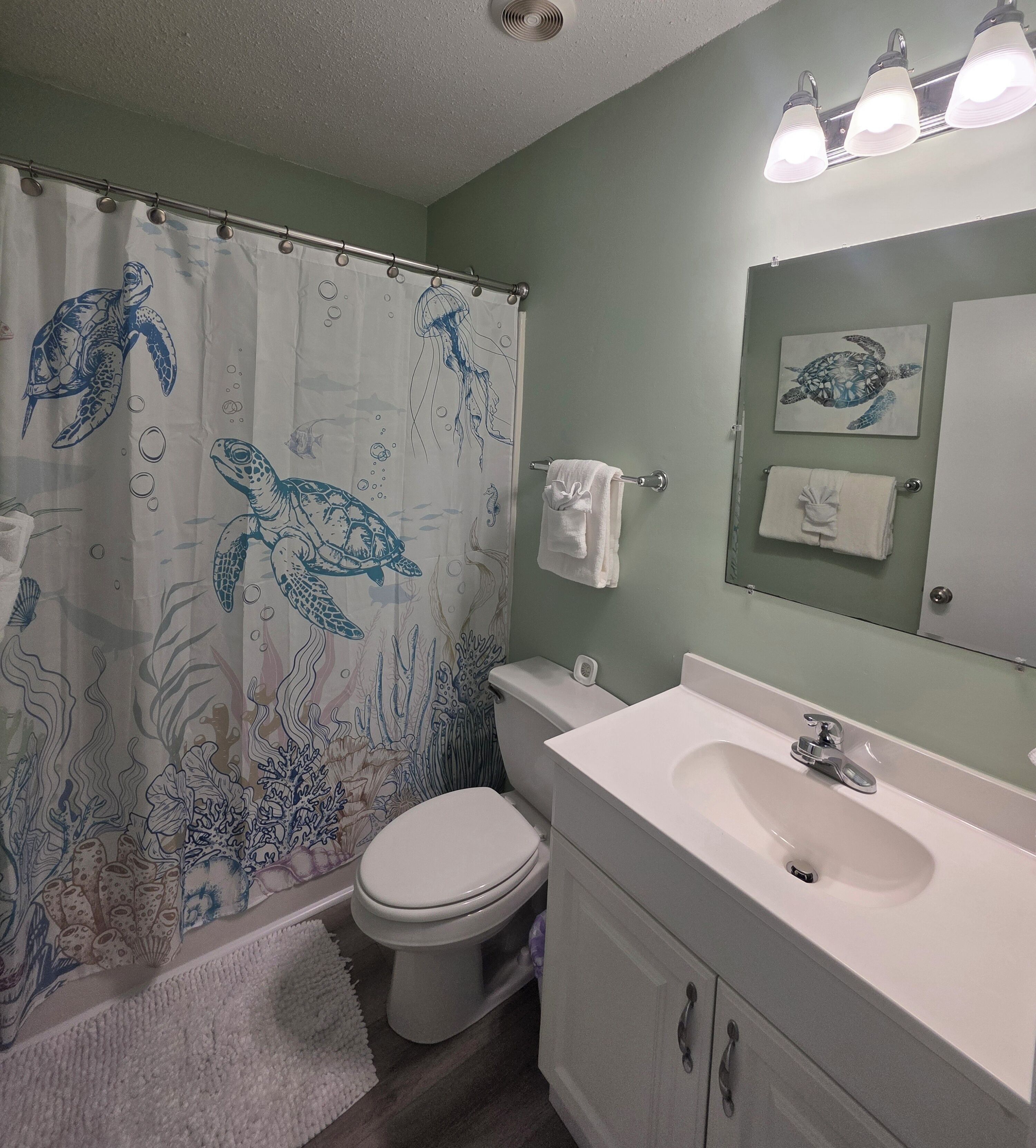 A bathroom with a shower curtain featuring sea creatures, a toilet, a sink with a mirror, and a towel rack.