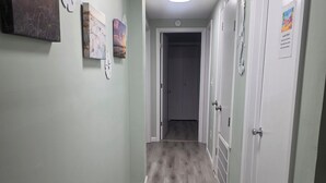 Corredor com paredes verde-claras, soalho de madeira e portas brancas. Há relógios fixados na parede e uma placa indicando uma lavandaria.