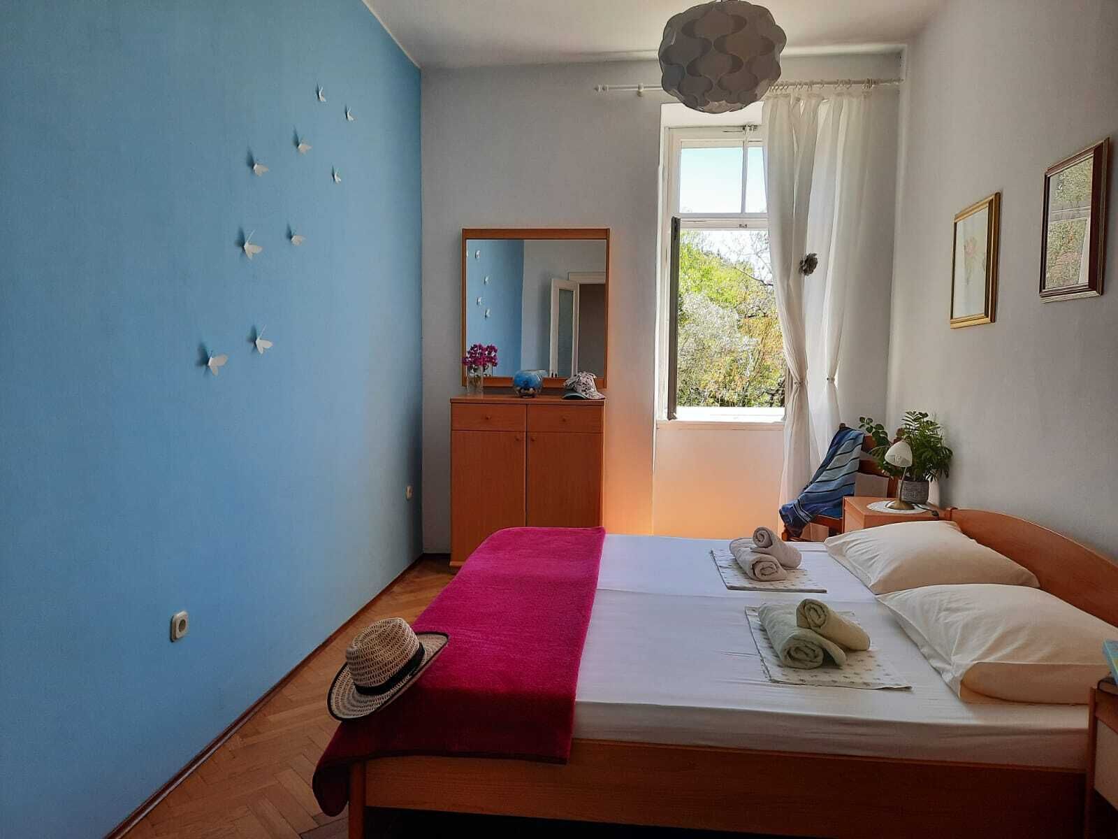 Quarto com uma cama, cômoda de madeira, espelho e janela com cortinas.