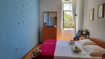 Quarto com uma cama, cômoda de madeira, espelho e janela com cortinas.