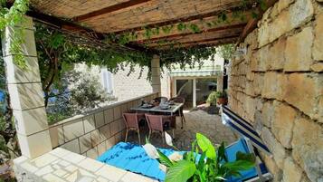 Un patio techado con una mesa y sillas, paredes de piedra y vista a la calle.