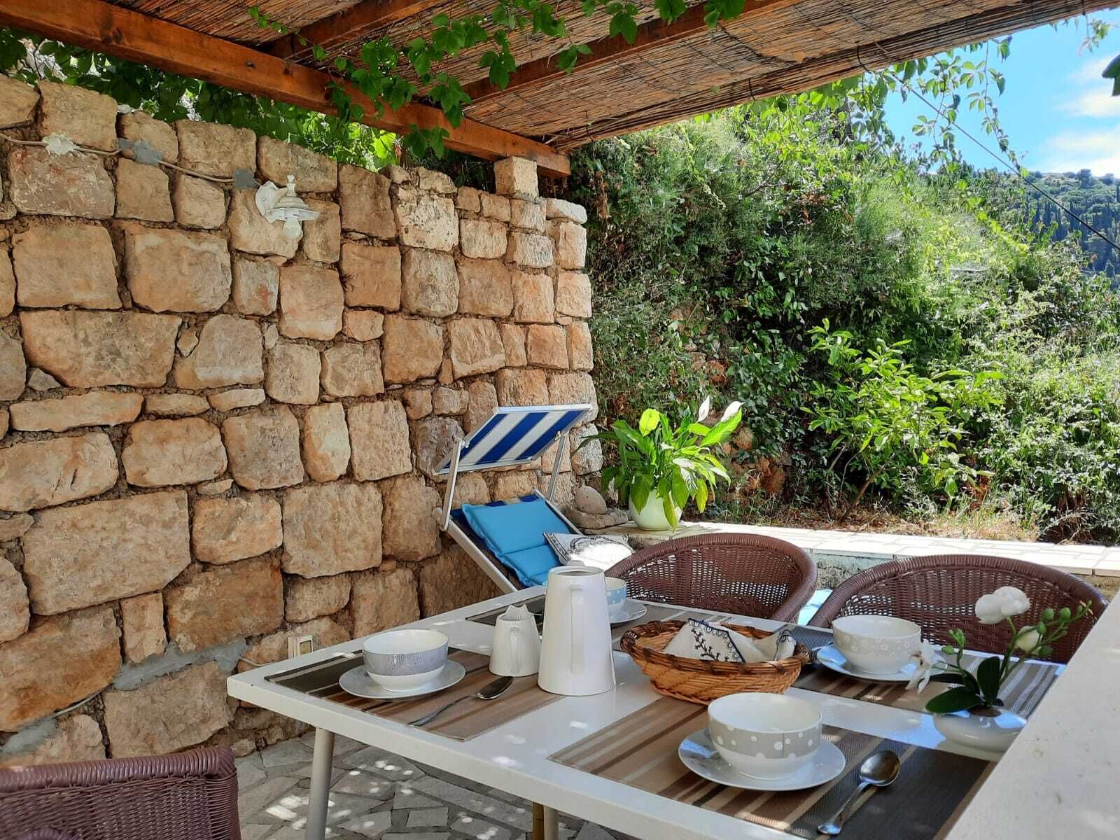 Un mur de pierre, une chaise à rayures bleues et une table en osier, le tout agrémenté d’assiettes, de tasses et d’un panier.