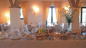 A dining area with tables set for a meal, featuring a variety of dishes and bread baskets.