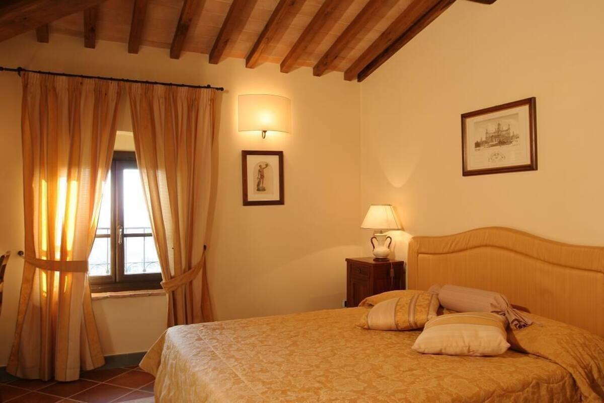 A bedroom with a bed, curtains, a nightstand, a lamp, and two framed pictures on the wall.