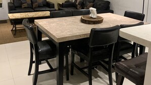 Ett modernt vardagsrum med en matplats, med en stor soffgrupp, ett matbord med stolar och en liten hylla med dekorativa föremål.