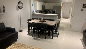 Ett modernt vardagsrum med en matplats, en svart soffa, ett soffbord och ett kök i bakgrunden.