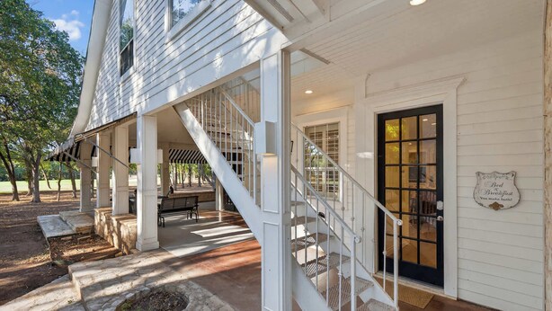 A white building with a covered porch, a staircase, and a door with a sign.