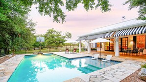 A swimming pool with stone tiles, surrounded by a fence and trees.