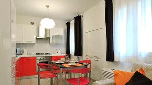 A compact kitchen with red cabinets, a dining table with four red chairs, and a modern pendant light. - Red House ai Mori (Venice)