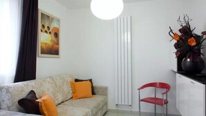 A modern living room with a sofa, a red chair, a white radiator, and a painting on the wall. - Red House ai Mori (Venice)
