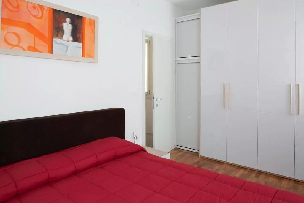 Een slaapkamer met een rood beddegoed, een witte garderobe en een schilderij aan de muur.