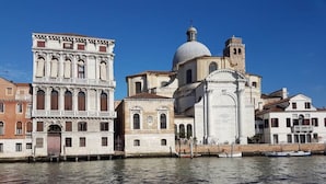 A historic building with a prominent dome and bell tower, adjacent to a canal with a boat. - Corte dei Bari (Venice)