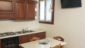 A kitchen with wooden cabinets, a gas stove, a sink, and a dining table with chairs. - Corte dei Bari (Venice)