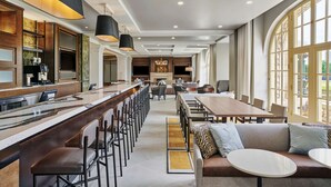 A modern hotel lobby with a long bar, seating area, and large windows.