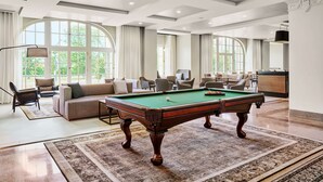 A spacious living room with a pool table, comfortable seating, large windows, and a modern ceiling design.