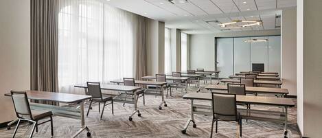A conference room with tables and chairs, large windows with curtains, and a carpeted floor.