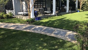 Una casa moderna con un porche cubierto, mobiliario de exterior y un césped bien cuidado.