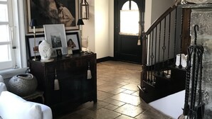 Un salón amplio con suelo de baldosas de piedra, un sofá blanco, un aparador de madera oscura y una araña.