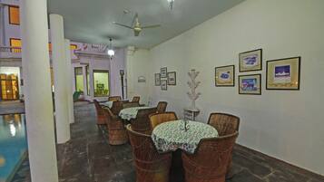 Un comedor con sillas y mesas de mimbre, una piscina y cuadros en la pared.