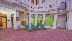 A hotel lobby with a curved balcony, green lounge chairs, and a red-tiled floor. - The Hadoti Palace (Bundi)