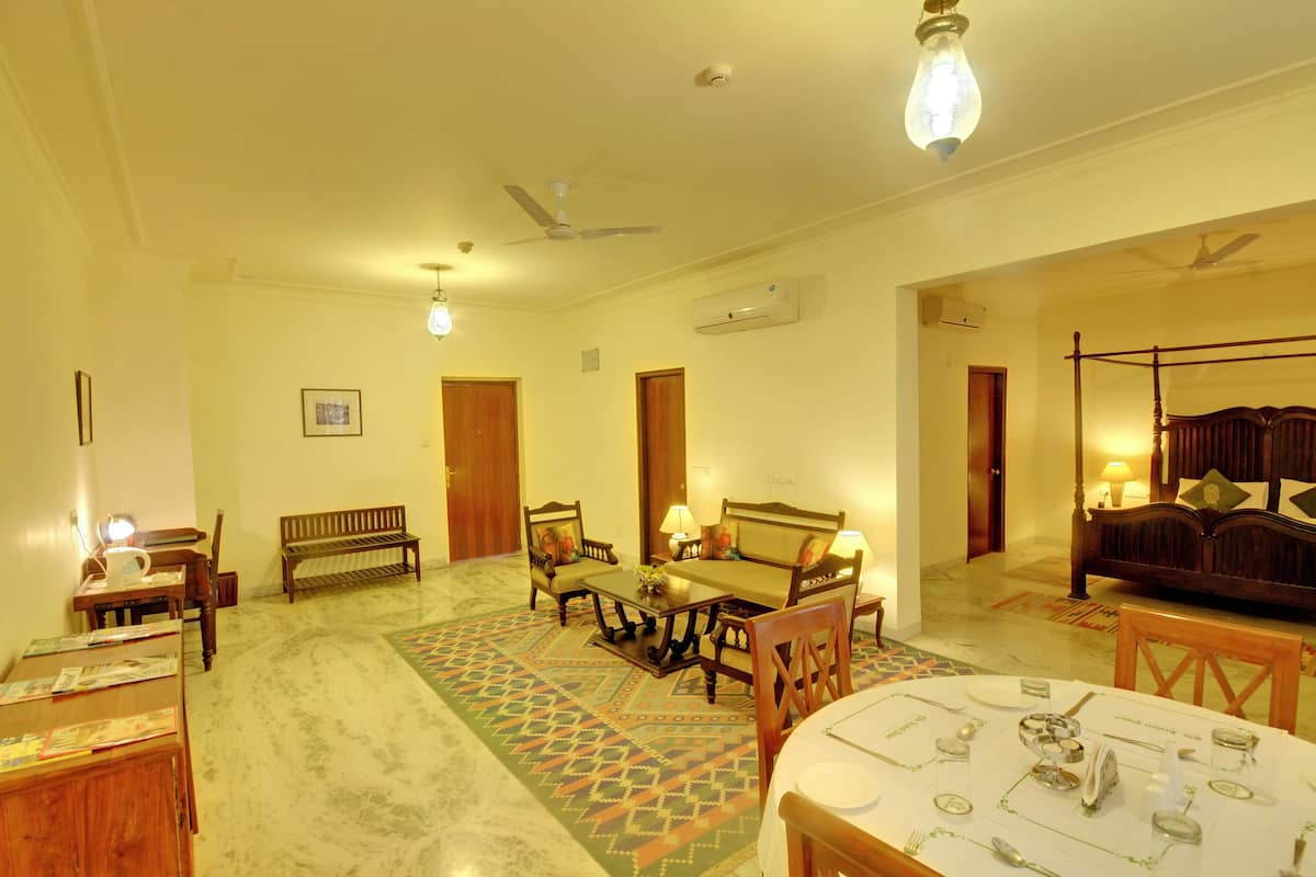 Quarto bem iluminado com mesa de jantar posta para quatro, sofá, banqueta e cama de dossel.