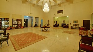 A spacious lobby with a chandelier, ceiling fans, and a large rug. - The Hadoti Palace (Bundi)