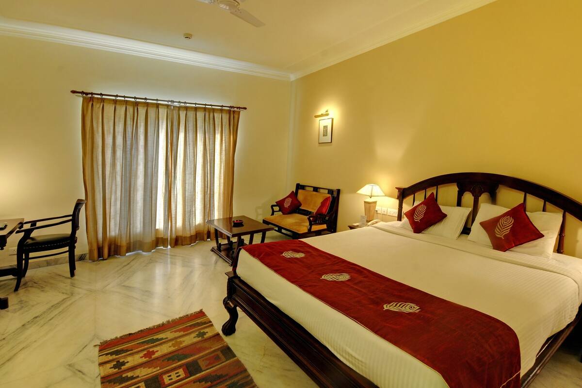 Quarto de hotel com uma cama grande, uma escrivaninha, uma cadeira e uma janela com cortinas.