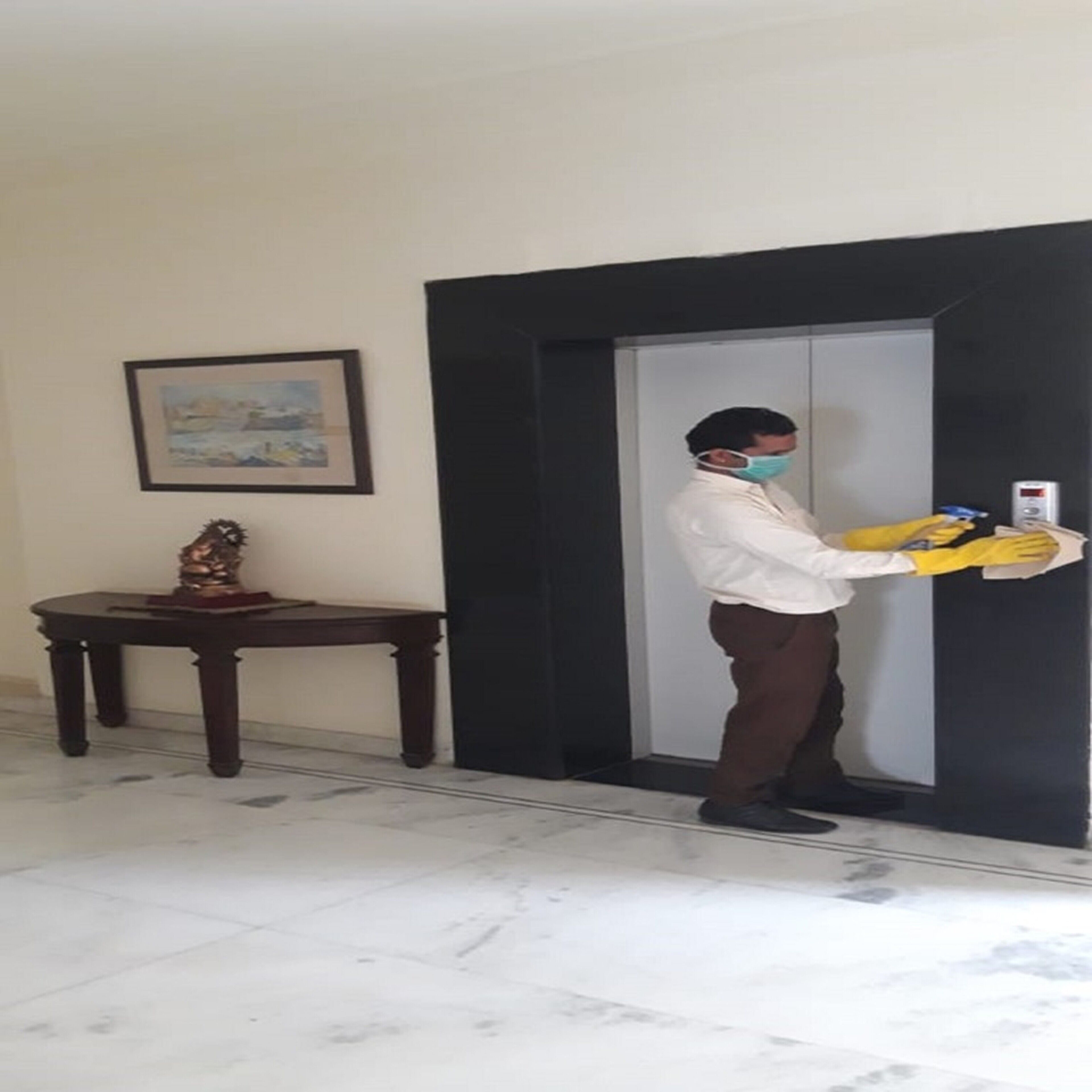 A person in a white shirt and brown pants standing in a hallway, holding a yellow object near a door.