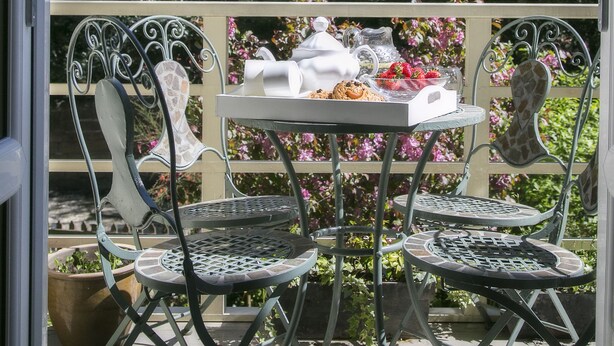 Eine Terrasse im Freien mit Metallstühlen und einem Tisch, gedeckt mit einem Teekessel, Tassen und einer Karaffe.