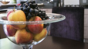 Eine Küche mit hellen Schränken, einer dunklen Spritzschutzwand und einer Obstschale auf der Arbeitsplatte.