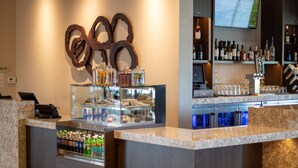 A bar area with a marble counter, a refrigerated display case with beverages, and a wall-mounted decorative piece. - Hyatt Place Altoona/Des Moines (Altoona)