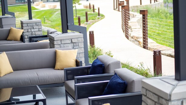 An outdoor seating area with sofas and tables, stone pillars, and a pathway leading to a building. - Hyatt Place Altoona/Des Moines (Altoona)