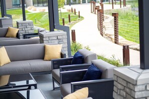An outdoor seating area with sofas and tables, stone pillars, and a pathway leading to a building. - Hyatt Place Altoona/Des Moines (Altoona)