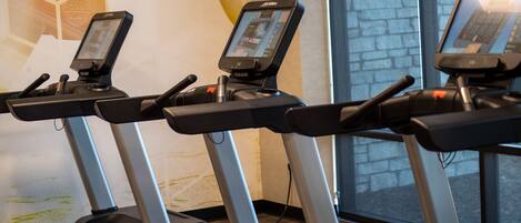 Three stationary bikes with digital screens, a stone wall, and a window with a view.
