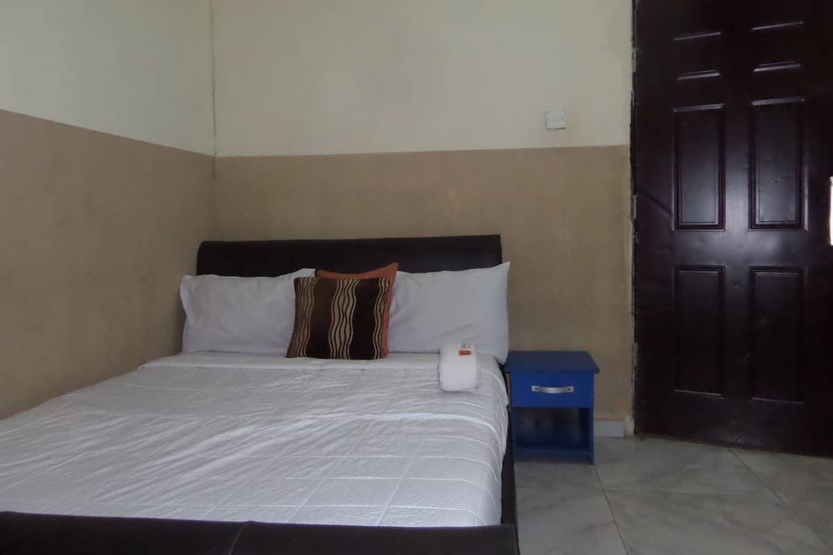 A bedroom with a bed, pillows, a nightstand, and a door.