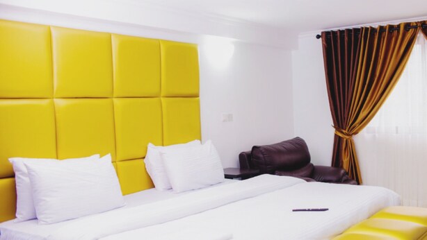 A hotel room with a large bed, a headboard, a bedside table, and a window with curtains. - Ivon Suites (Lagos)