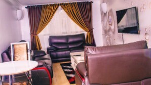 A modern living room with a leather sofa, a dining table, and a TV mounted on the wall. - Ivon Suites (Lagos)